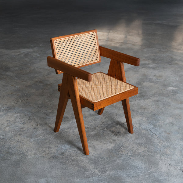 Stylish wooden armchair with a mid-century modern design, featuring a natural cane seat and backrest, placed on a textured concrete floor in a minimalist setting.