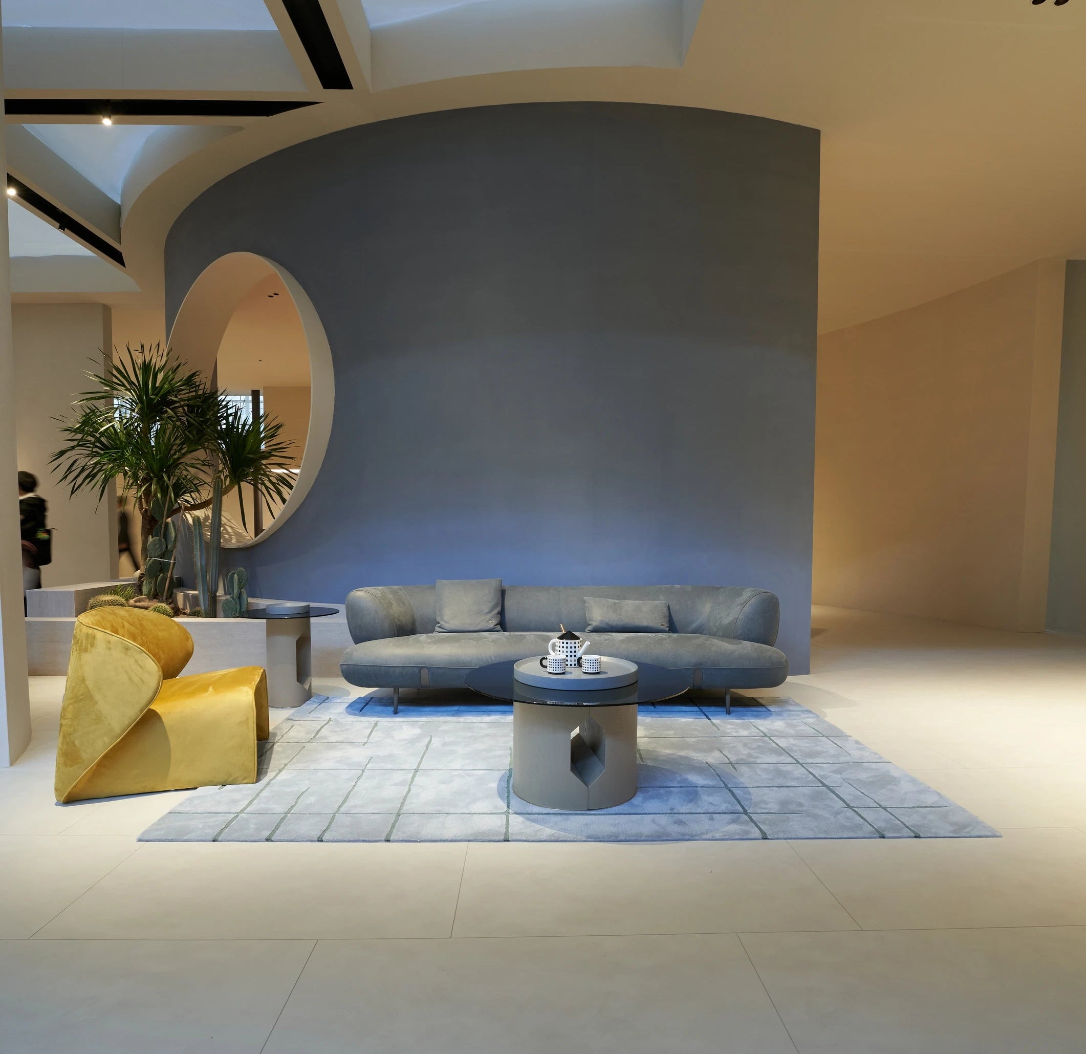 Modern living room with a gray leather sofa, yellow chair, and round window.