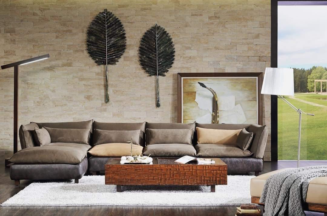 Contemporary living room with dark brown sectional sofa, wooden coffee table, modern floor lamps, and textured wall art on a neutral stone backdrop.